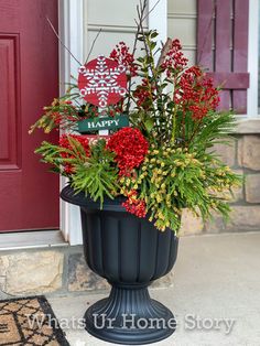 a planter filled with red flowers and greenery on the front steps of a house