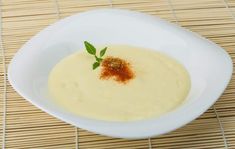 a white bowl filled with soup sitting on top of a wooden table next to a bamboo mat