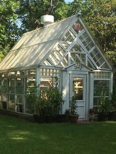 a small white greenhouse sitting in the middle of a yard with potted plants on it