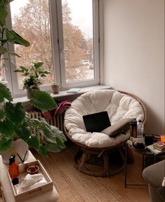 a laptop computer sitting on top of a wooden chair in a living room next to a window