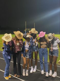 five girls in cowboy hats standing on the side of a road at night with their backs turned to the camera