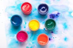 six different colors of paint sitting on top of a blue and white paper covered in watercolor