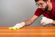 a man in red shirt and white gloves cleaning wooden table with yellow sponge on it