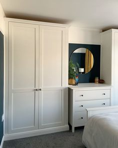 a white bed sitting next to a tall white cabinet with mirror on top of it