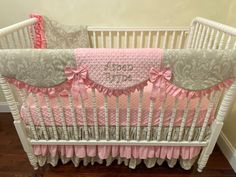 a baby crib with pink and gray bedding on the bottom, along with matching pillows