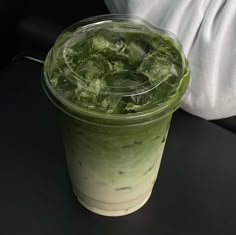 there is a green drink with ice on the table next to a white cloth and a person's arm behind it