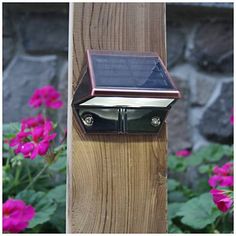 a solar powered light mounted on the side of a wooden post in front of pink flowers