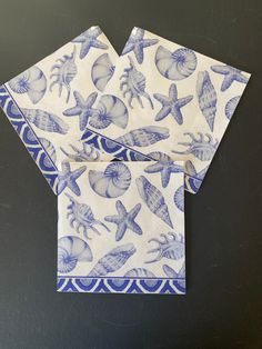 two blue and white napkins with seashells on them sitting on a black surface