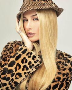 a woman with long blonde hair wearing a leopard print coat and wide brimmed hat