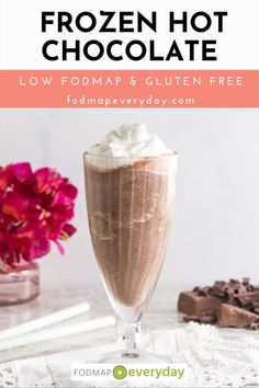 a glass filled with chocolate and whipped cream on top of a white table next to pink flowers