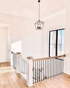 an empty living room with wood floors and white walls, chandelier hanging from the ceiling