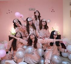 a group of women sitting on top of a pile of silver and pink balloons in front of a wall