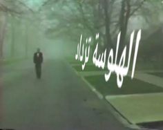 two people walking down the street in front of some trees and bushes with arabic writing on it