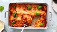 a casserole dish filled with lasagna sauce and basil garnished with cheese