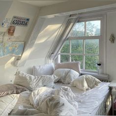 an unmade bed with white sheets and pillows in front of a window overlooking the trees