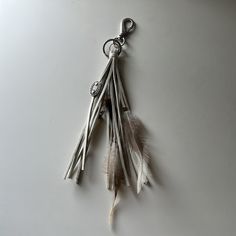 a feather keychain hanging from a hook on a white surface with other items attached to it