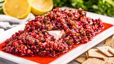 a plate topped with red rice next to crackers and lemon wedges