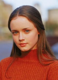 a woman with long hair wearing an orange turtle neck sweater and looking at the camera