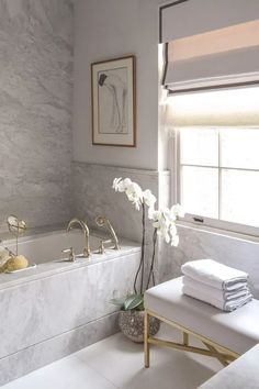 an instagramted photo of a bathroom with white marble and gold fixtures, including a bathtub