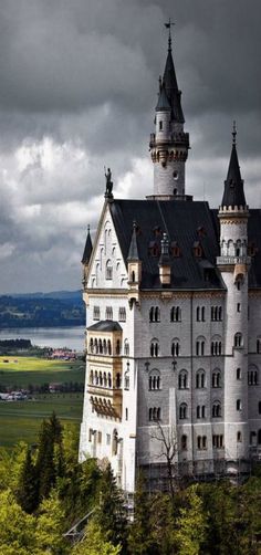 an old castle sits on top of a hill with trees in the foreground and dark clouds overhead