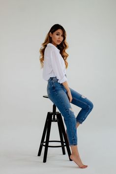 a woman sitting on top of a stool wearing jeans and a white button up shirt