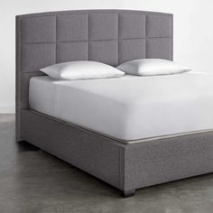 an upholstered bed with white pillows and gray linens is shown in this image