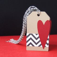 a tag with a red heart on it sitting on a table next to a black and white striped ribbon