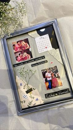 a silver frame with pictures and flowers on it sitting on a white cloth covered table