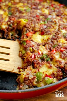 a skillet filled with food sitting on top of a wooden table next to a spatula