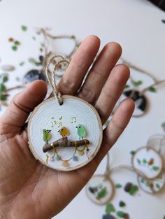 a hand holding a small ornament with birds on it's side and another bird in the background