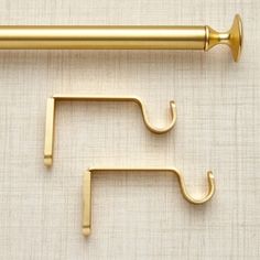 two gold metal hooks hang from the side of a curtain rod on a beige background