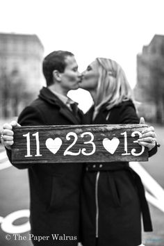 a man and woman kissing in front of a wooden sign that says i love you