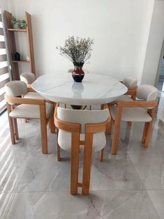 a white table with six chairs around it and a vase filled with flowers on top