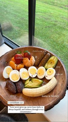 an assortment of fruits and vegetables on a wooden platter next to a large window