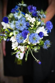 a bouquet of blue and white flowers is held by a woman's hand in a black dress