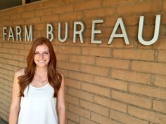 a woman standing in front of a brick wall with the word farm bureau on it