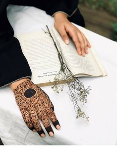 a woman is holding an open book on her left hand and wearing henna tattoos