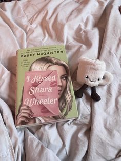 a stuffed animal next to a book on a bed with white sheets and pink covers