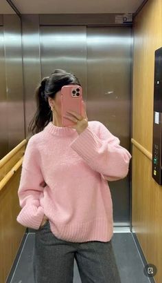 a woman taking a selfie in an elevator wearing a pink sweater and grey pants