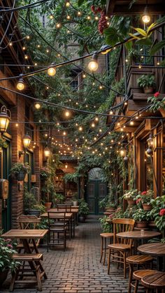 an alley way with tables and chairs covered in plants, lights and potted plants