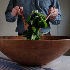 a man standing in front of a large wooden bowl filled with greens and chopsticks