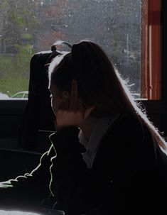 a woman sitting in front of a window talking on a cell phone while holding her hand up to her face