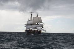 an old sailing ship in the middle of the ocean under a cloudy sky with dark clouds