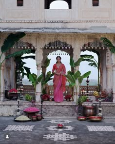 a woman in a pink sari standing on a porch with potted plants and decorations