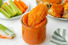 carrots and celery sticks sticking out of a jar filled with something orange