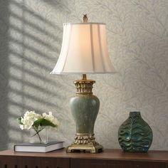 a lamp sitting on top of a wooden table next to a vase with white flowers