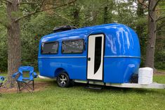 a blue and white trailer parked in the grass next to two chairs with one chair on it's side