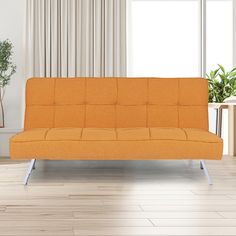 an orange couch sitting in front of a window next to a table and potted plant