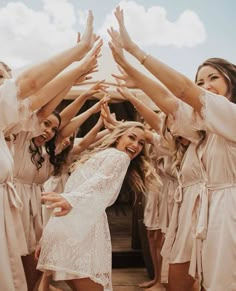 a group of women in white dresses holding their hands up to each other with their arms