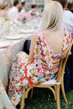 the back of a woman sitting at a table with flowers on it and people in the background